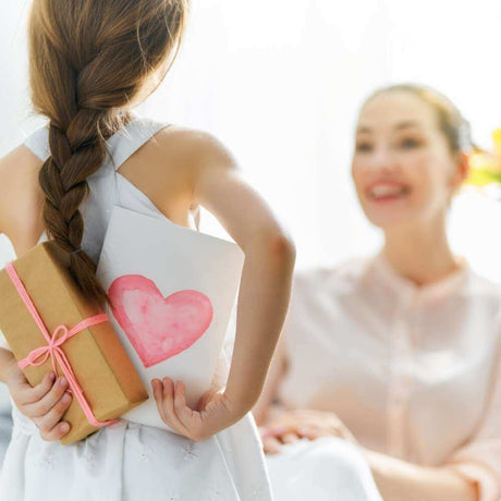 Child with mothers day gift & card behind her back in front of her mum