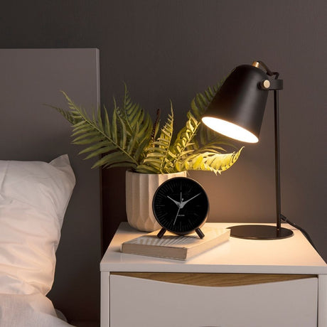 Alarm clock next to bed with plant and lamp