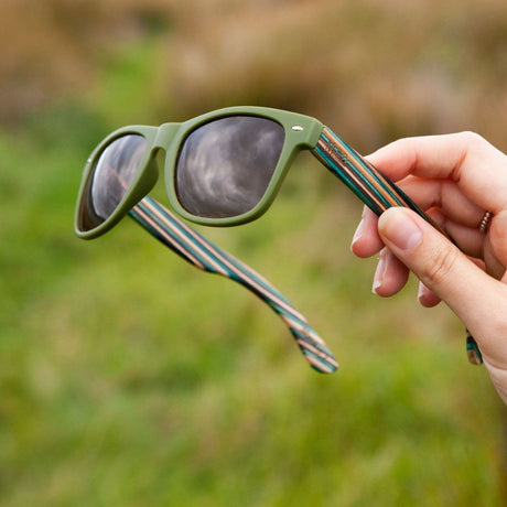 Hand holding sunglasses green background