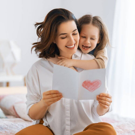 Mother Reading Mothers Day Card with Daughter cuddling her