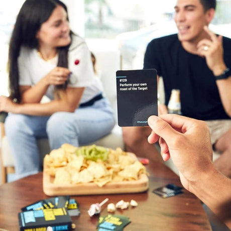 group of people playing a card game with pizza on table and person holding a card in foreground