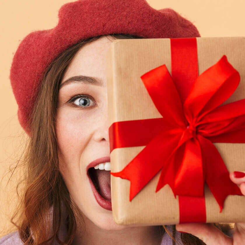 Woman holding wrapped gift in front of her face with red ribbon funky gifts nz